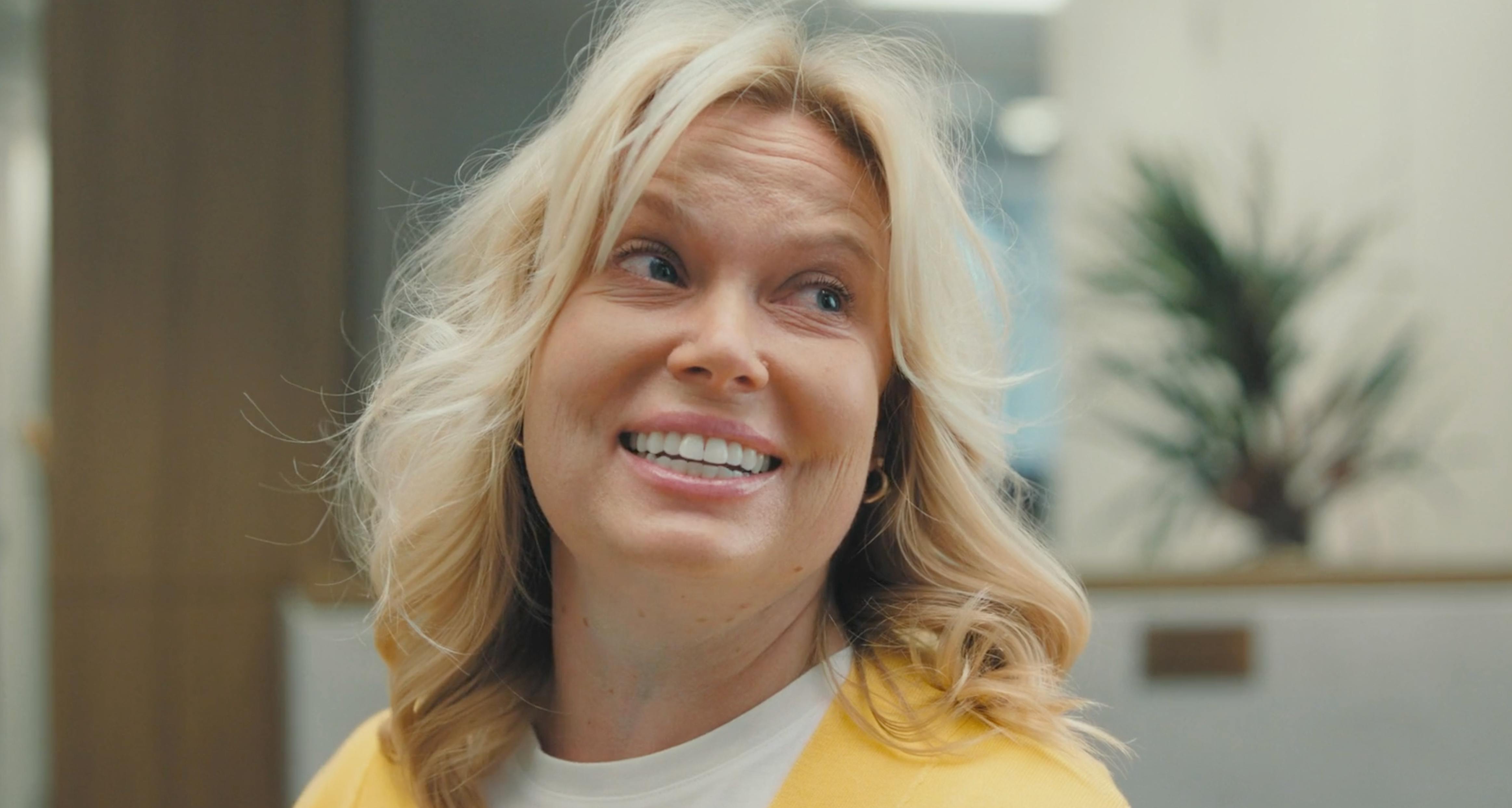 Macro lens close-up shot on a film set of a blonde woman in a yellow sweater smiling, showing natural skin texture and high-quality detail, useful in commercials and promotional video production.
