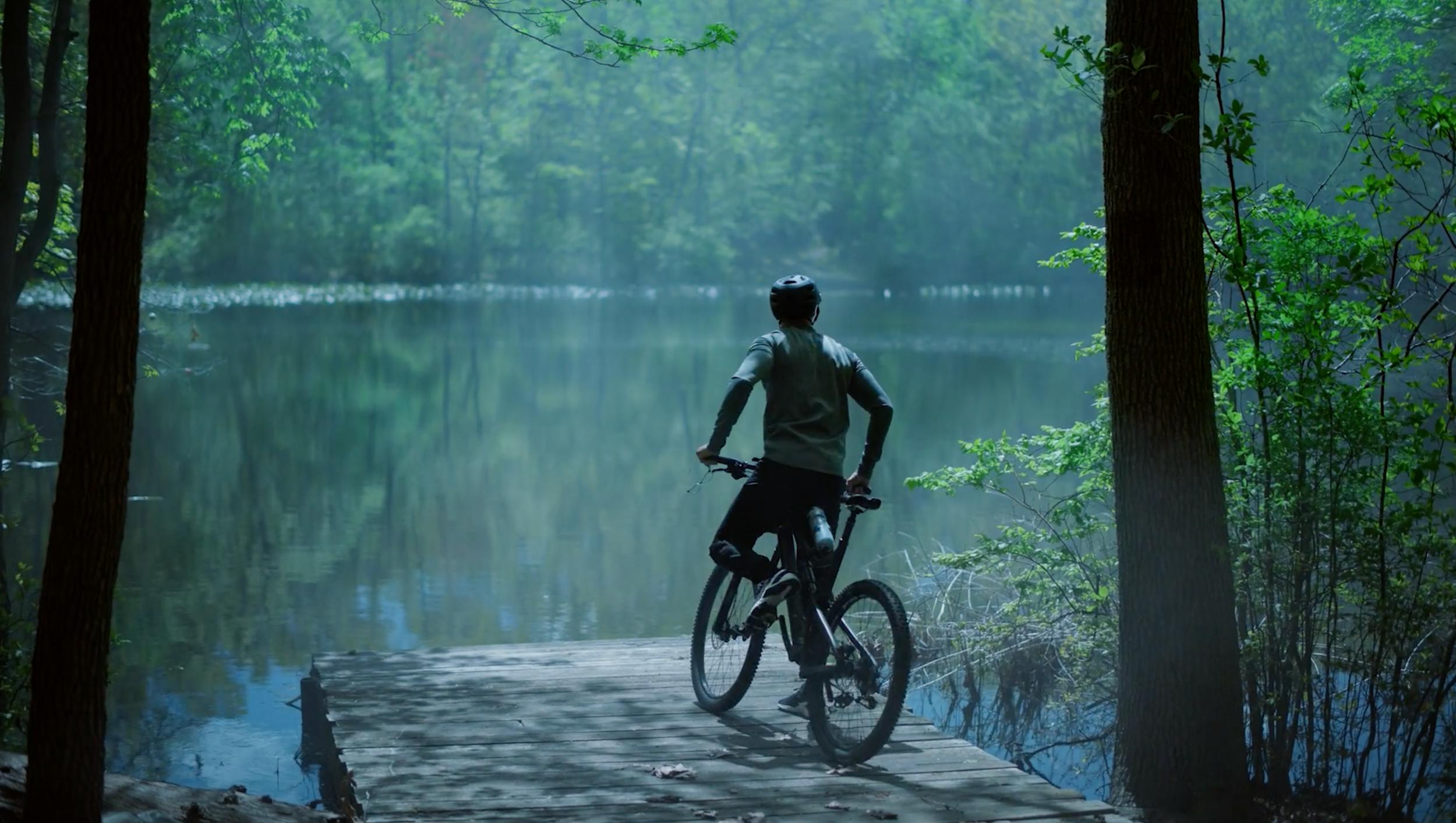 Cyclist pausing near a peaceful lake surrounded by nature, representing adventure, calmness, and outdoor lifestyle.