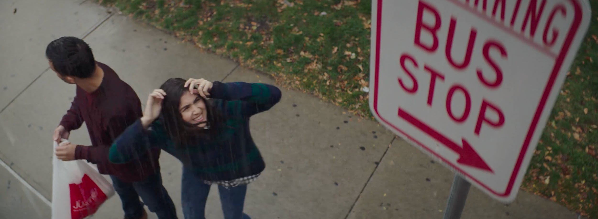 Two people standing near a bus stop sign outdoors, capturing everyday moments and lifestyle storytelling in video production