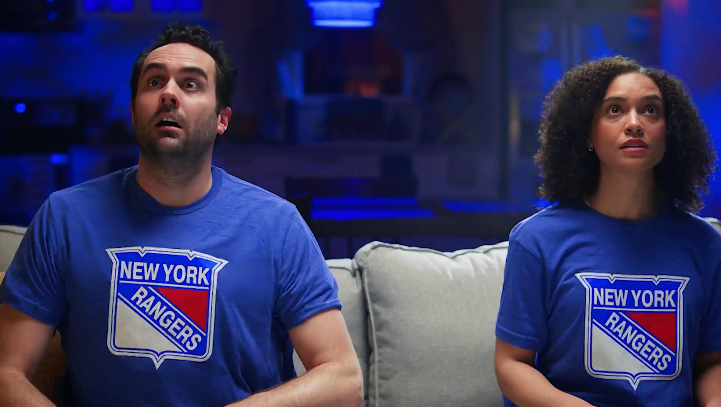 Two people wearing New York Rangers shirts reacting while watching TV, capturing audience engagement and sports storytelling in cinematic video production