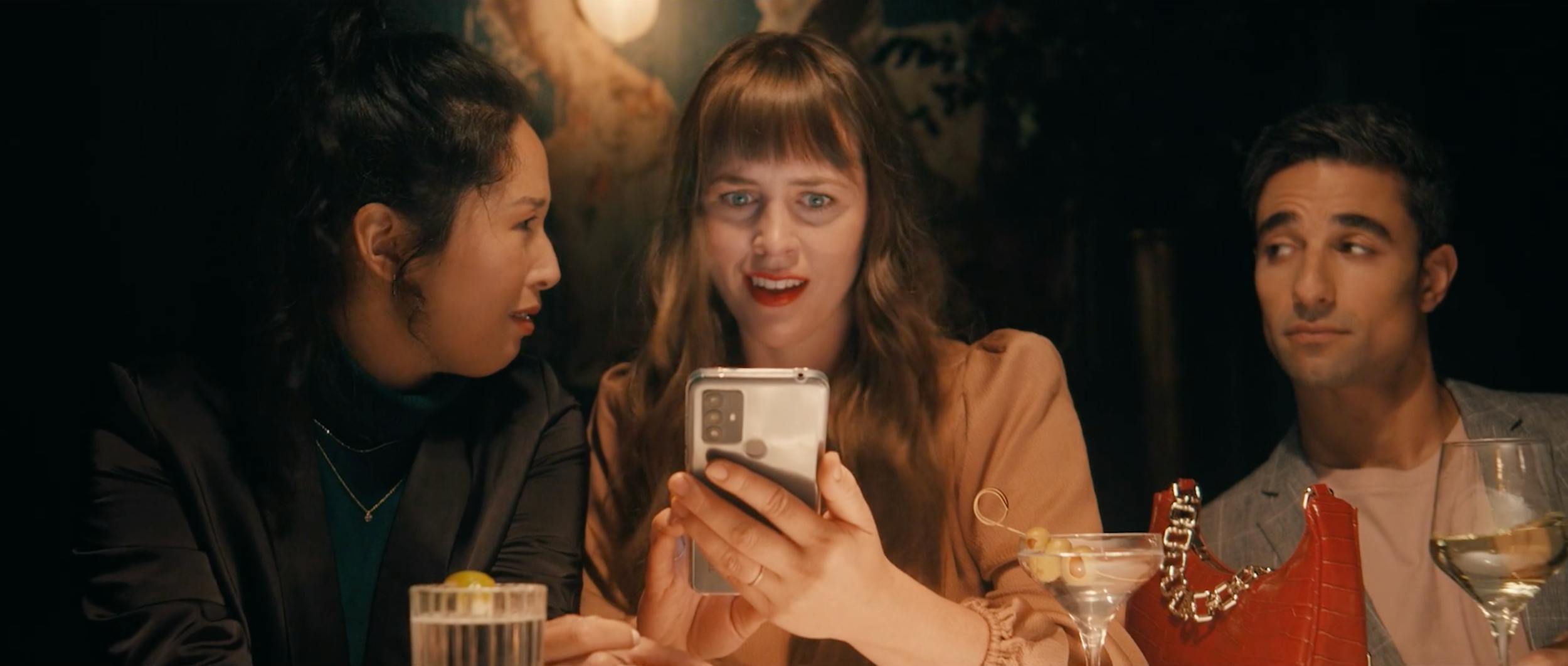 Friends gathered at a dinner table reacting to content on a smartphone, showcasing social connection and real-life engagement moments.