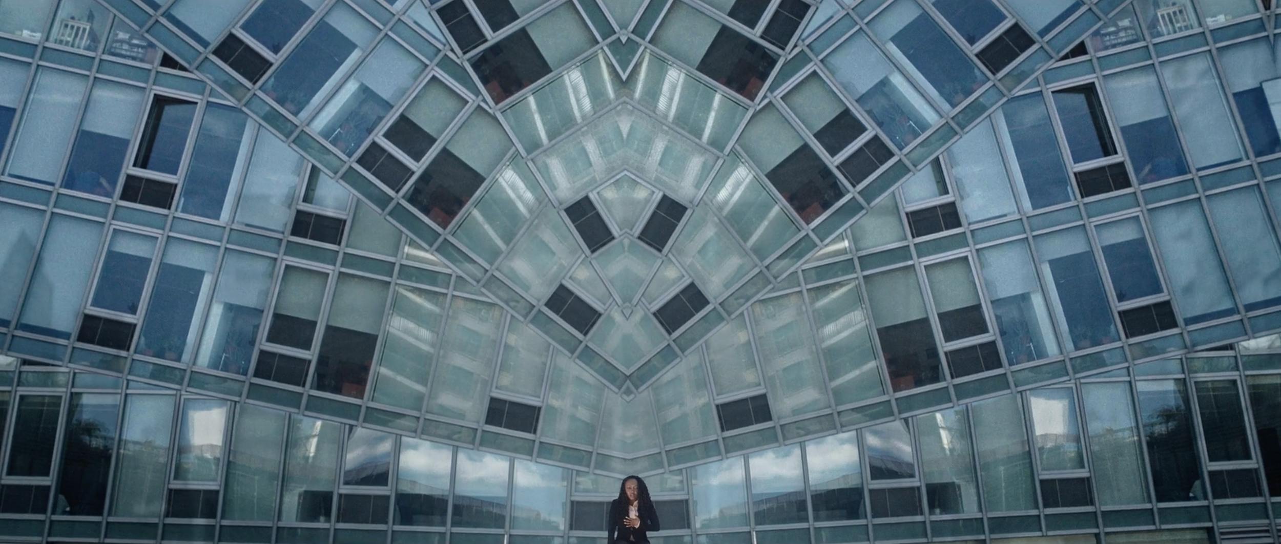 Symmetrical composition on a film set, with a person reflected in a modern glass facade, illustrating high-concept set design and unique camera perspectives in dynamic video production.
