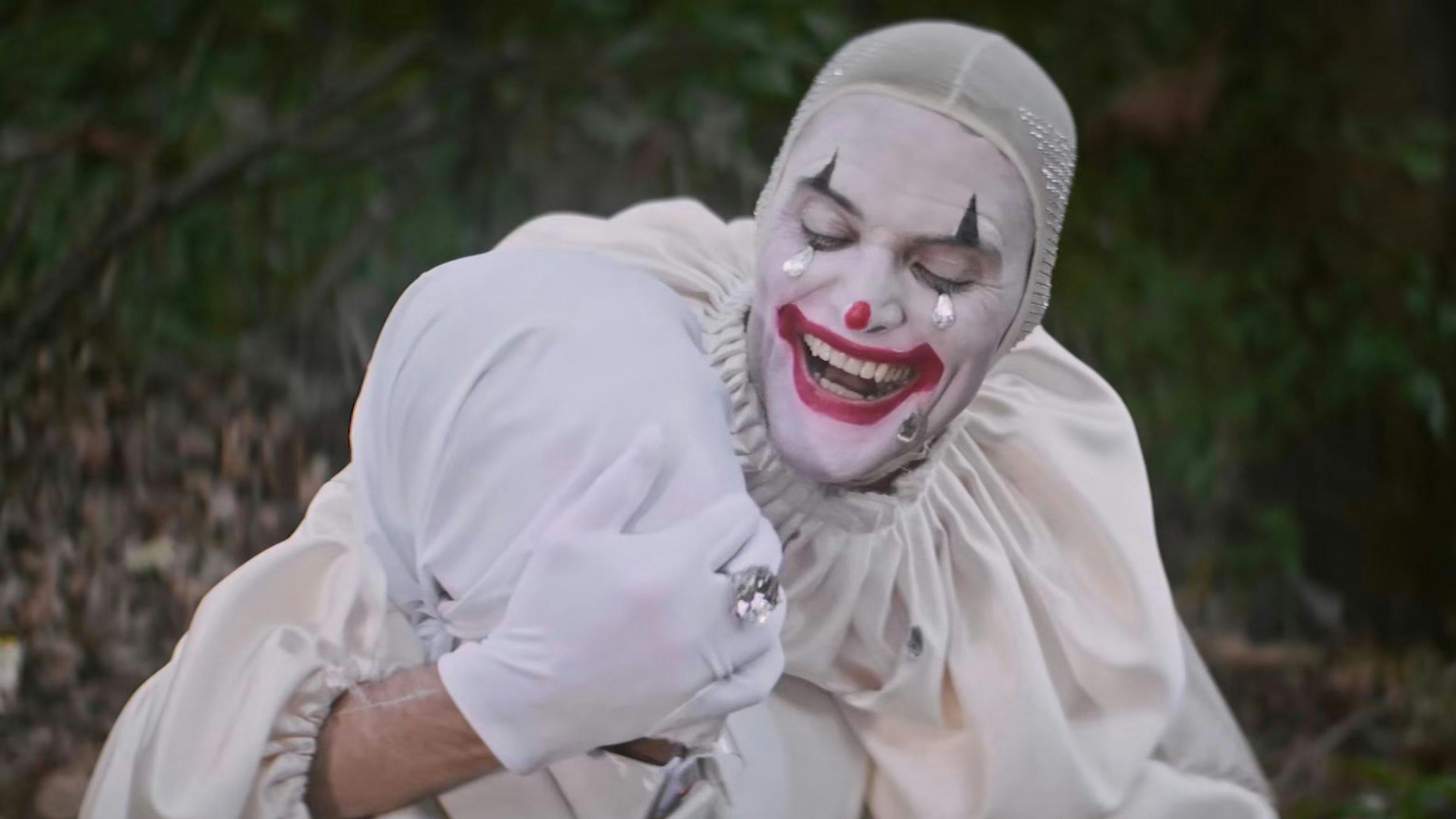 Close-up of a theatrical clown in whiteface makeup laughing. High-key lighting captures detailed costume textures and expressive performance, ideal for character-driven narrative film.