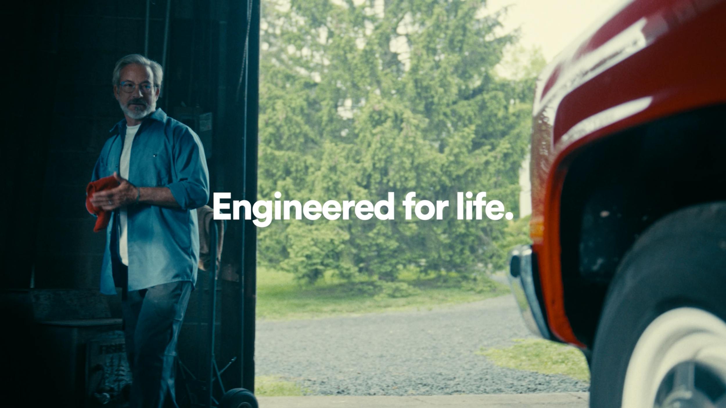 Man standing near garage with vehicle and text “Engineered for life,” representing brand storytelling and commercial video production scenes