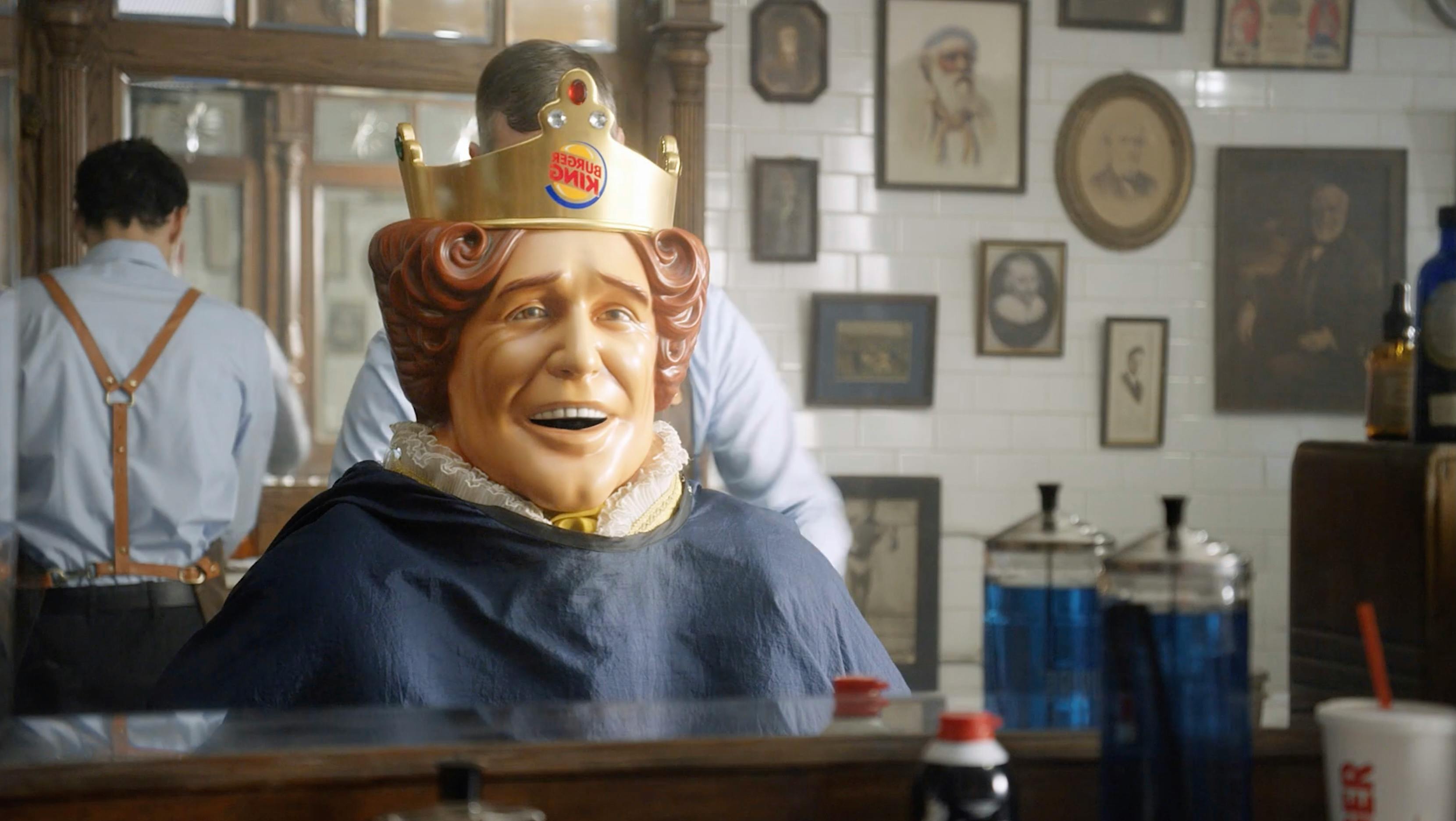 A person wearing a Burger King crown and a gold cape, standing in a room filled with framed photos.