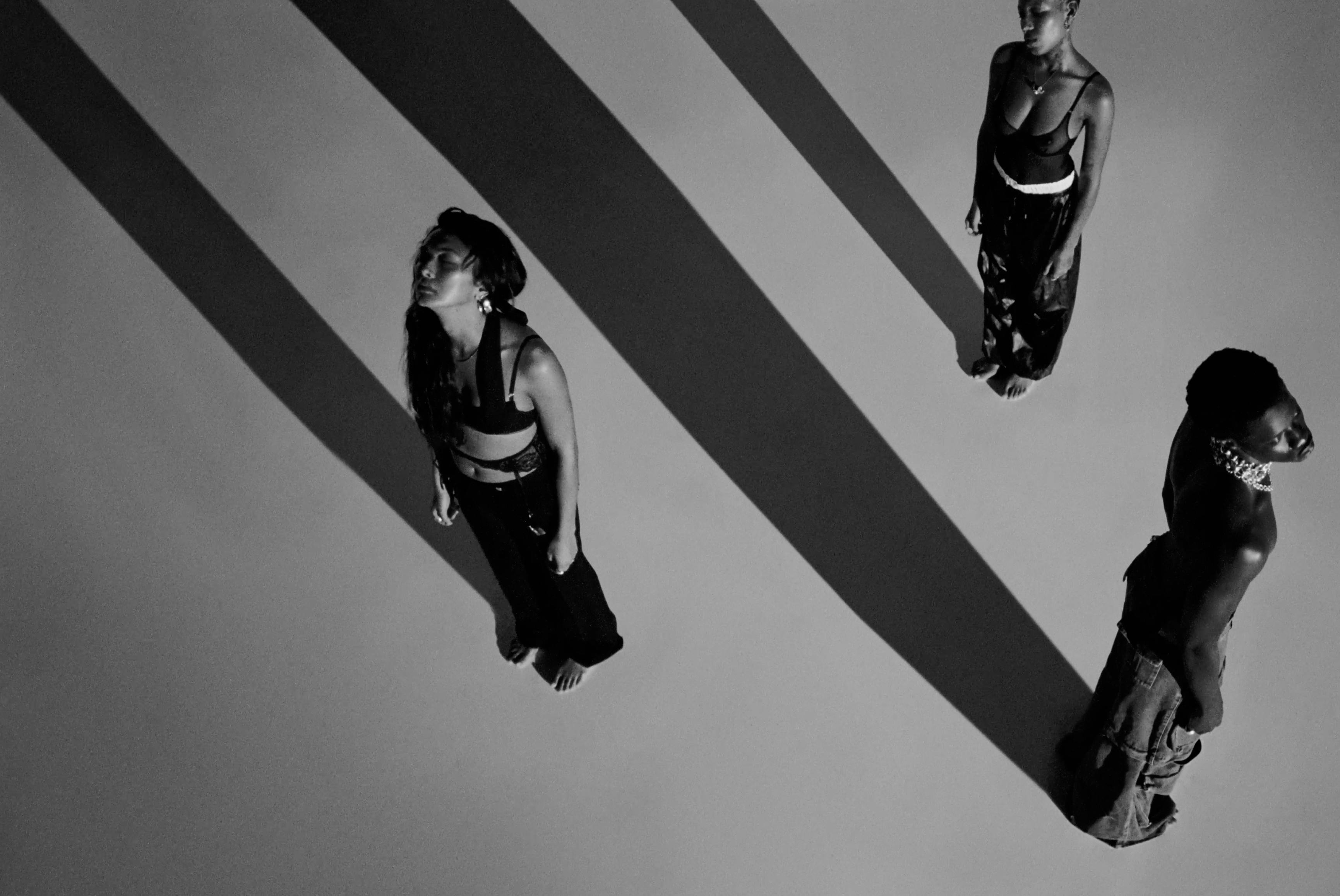 A high-angle, black-and-white shot of two people walking across a surface with long, dramatic shadows.