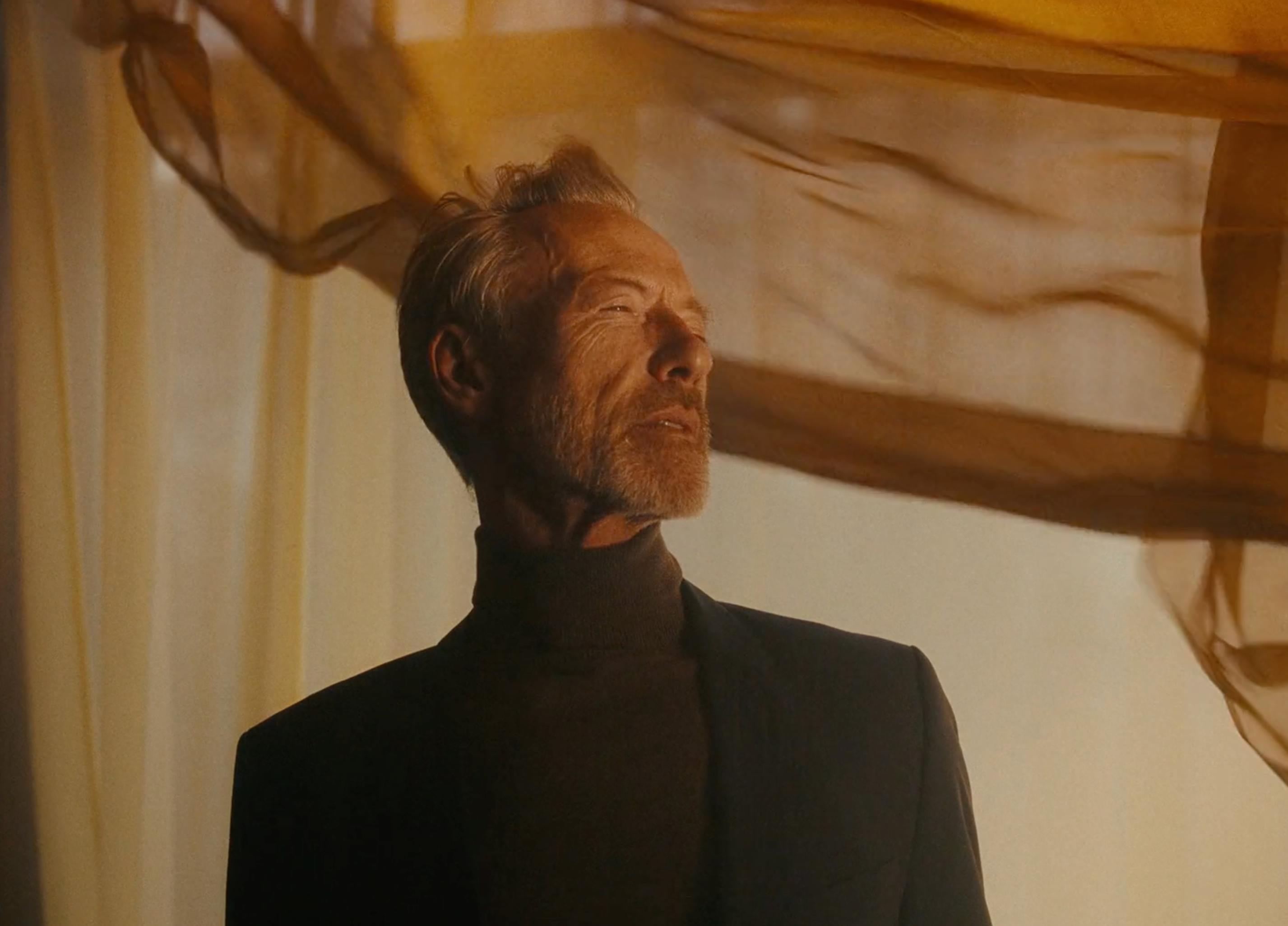 A man in a dark suit looking upwards in a grand, indoor setting.