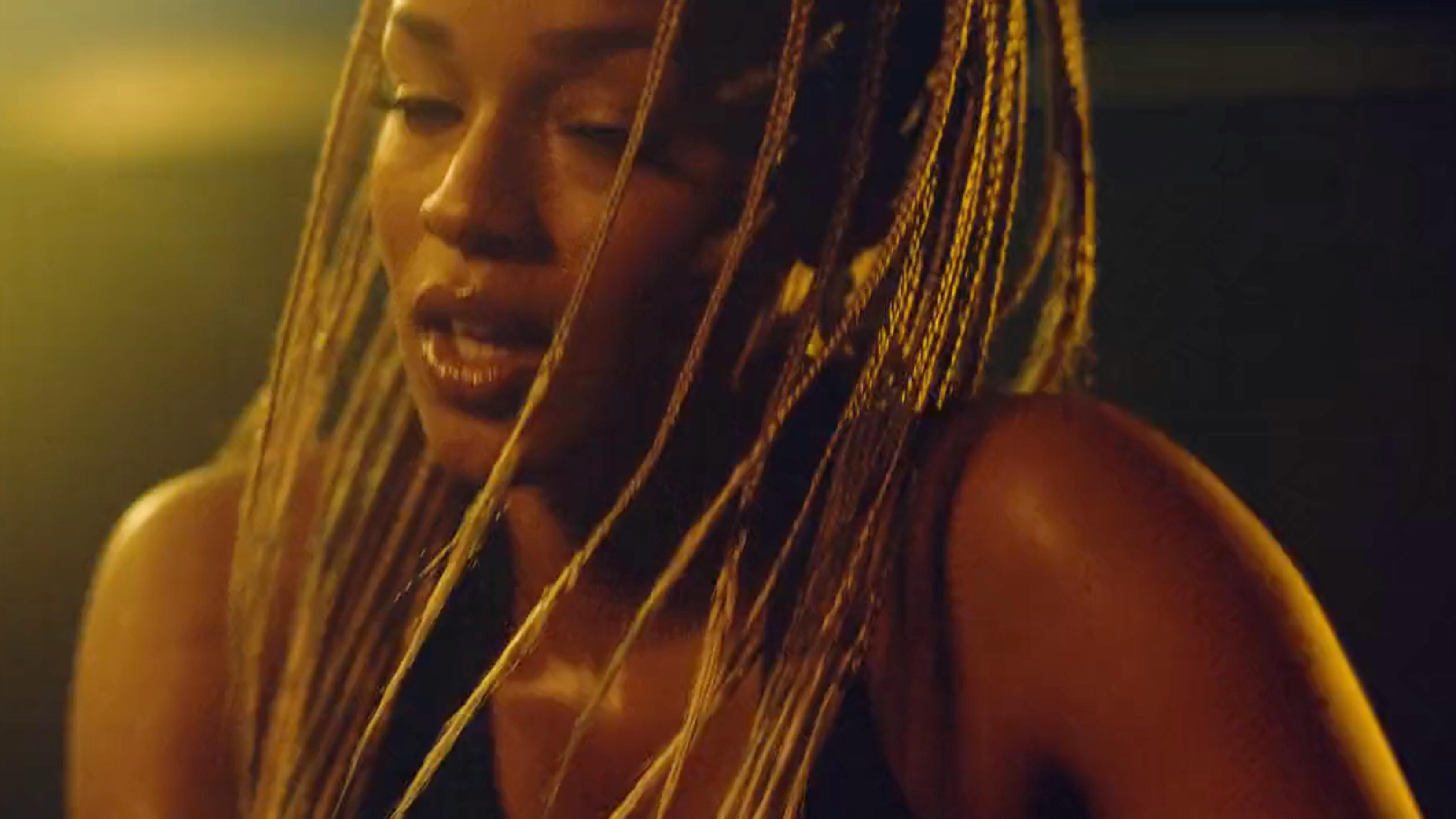 Close-up (CU) portrait of a woman with long, golden-blonde box braids. The scene uses warm, cinematic golden hour lighting that creates a soft glow on her skin and highlights the texture of her hair. The shallow depth of field creates a creamy, dark bokeh background.