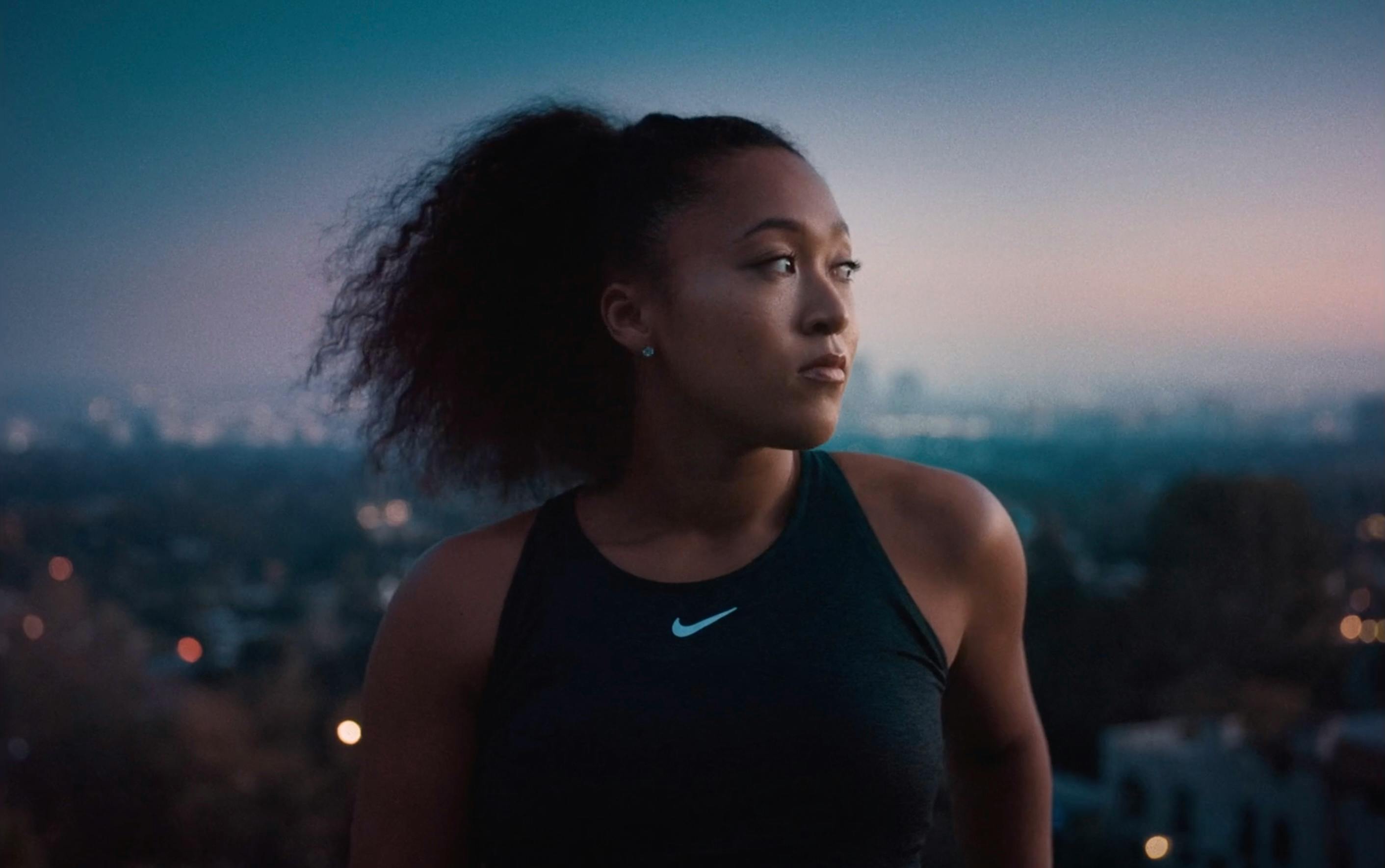 A focused, low-light portrait of Naomi Osaka in athletic wear.