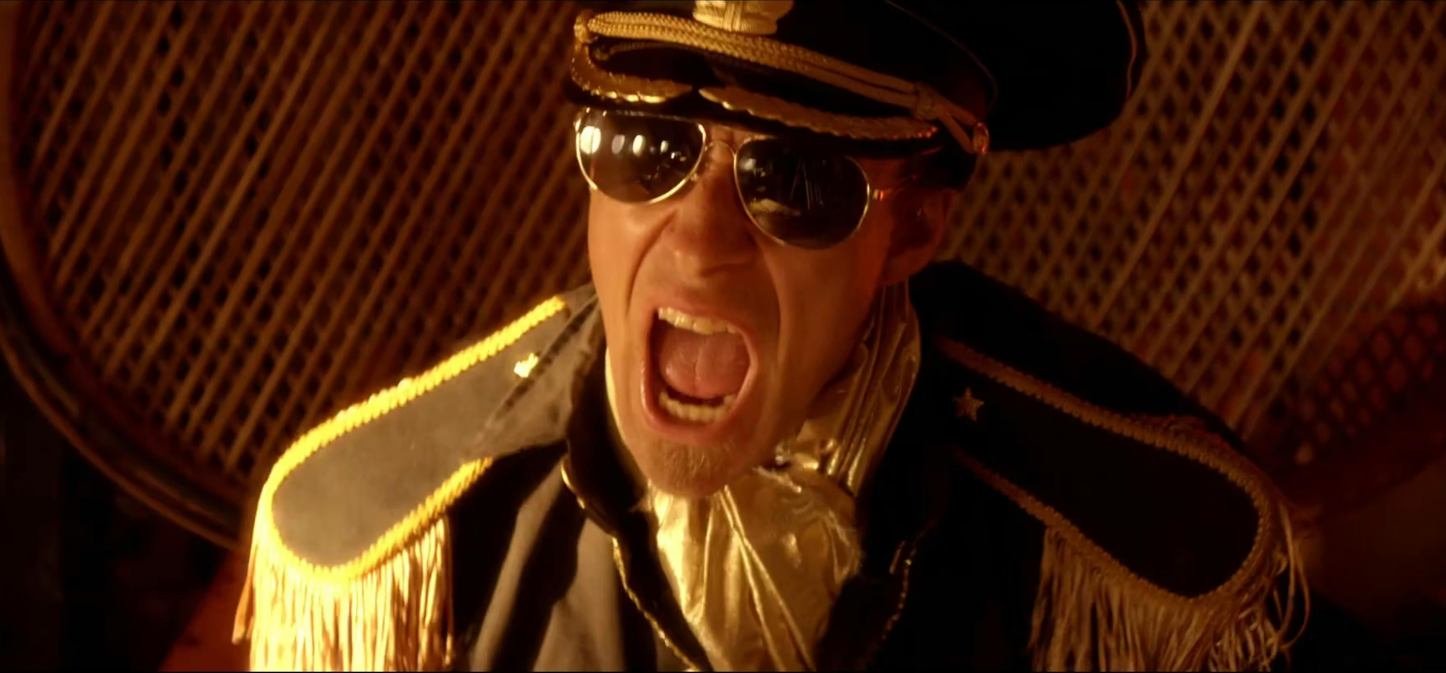 A high-energy, close-up shot of a person wearing sunglasses and screaming into a microphone.