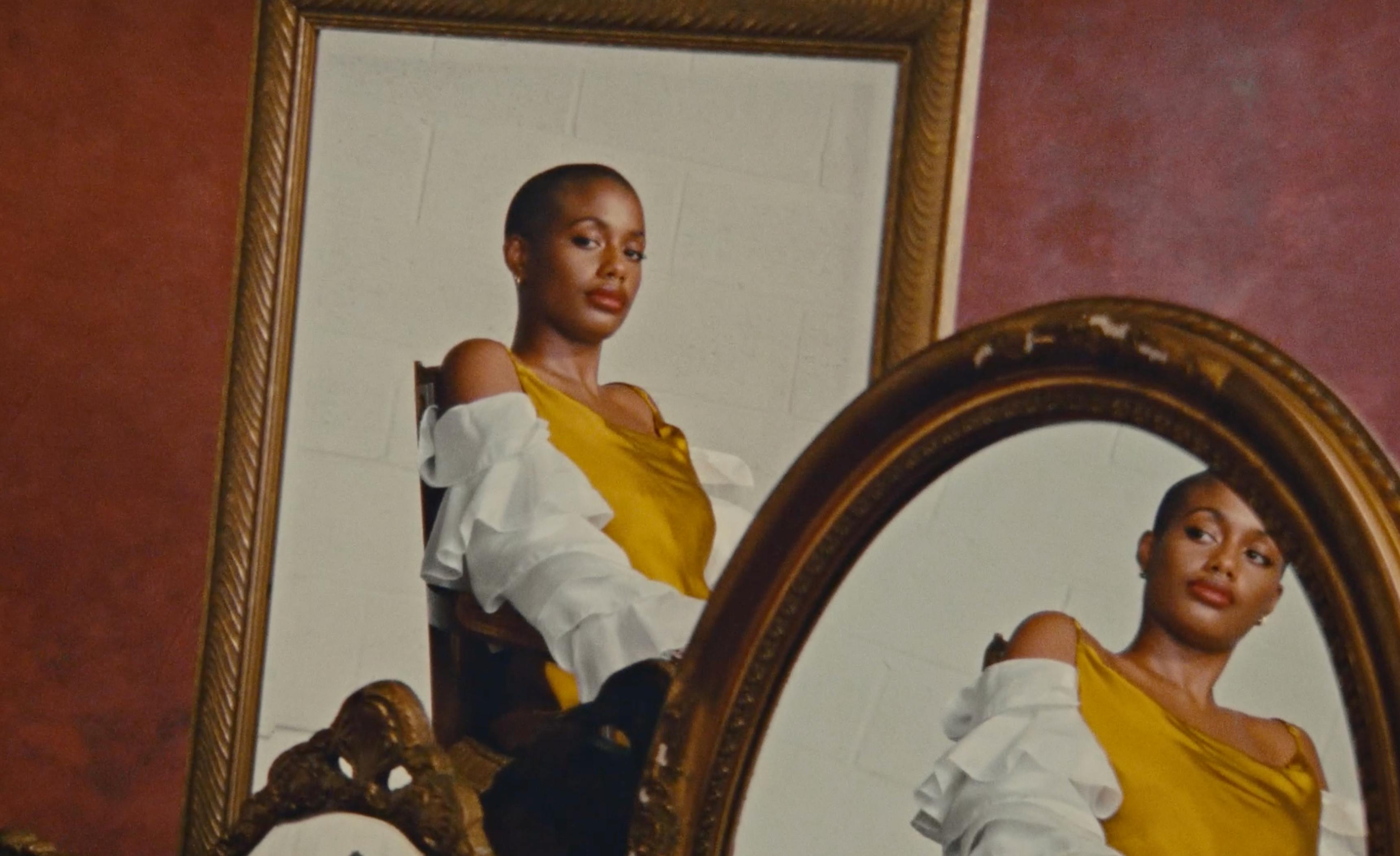 A shot of a framed portrait of a person leaning against a wall next to a circular mirror.