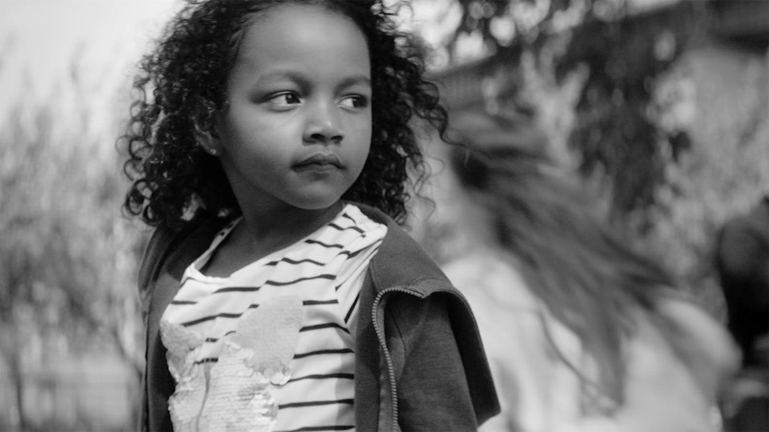 Black and white close-up of a young girl looking off-camera. Moody, high-contrast monochrome cinematography emphasizing raw emotion and narrative storytelling for a documentary or drama.