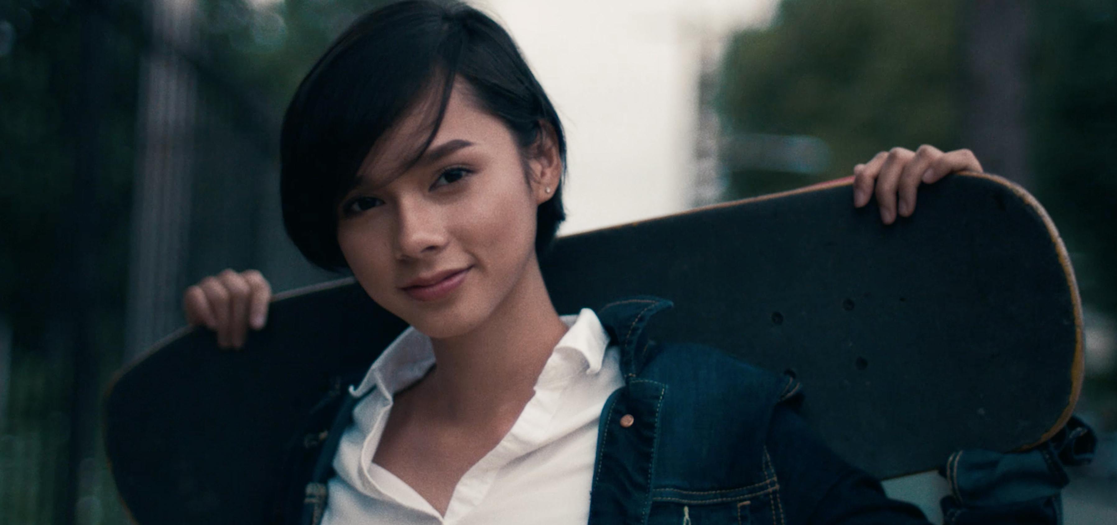 A portrait of a woman with dark hair wearing a white shirt, smiling gently at the camera against a soft-focus background.