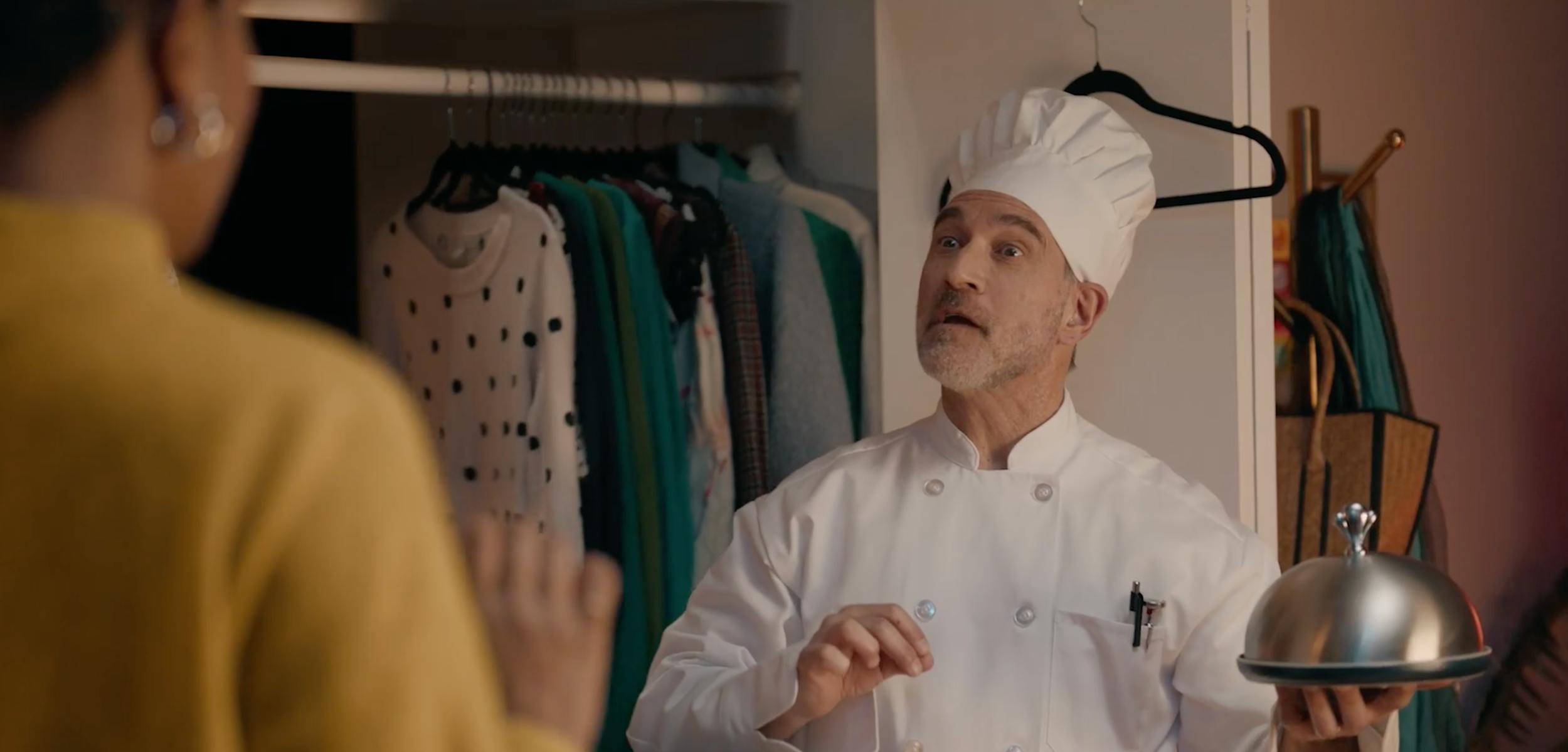 Chef standing in a closet holding a serving tray, creating a humorous and unexpected storytelling moment.