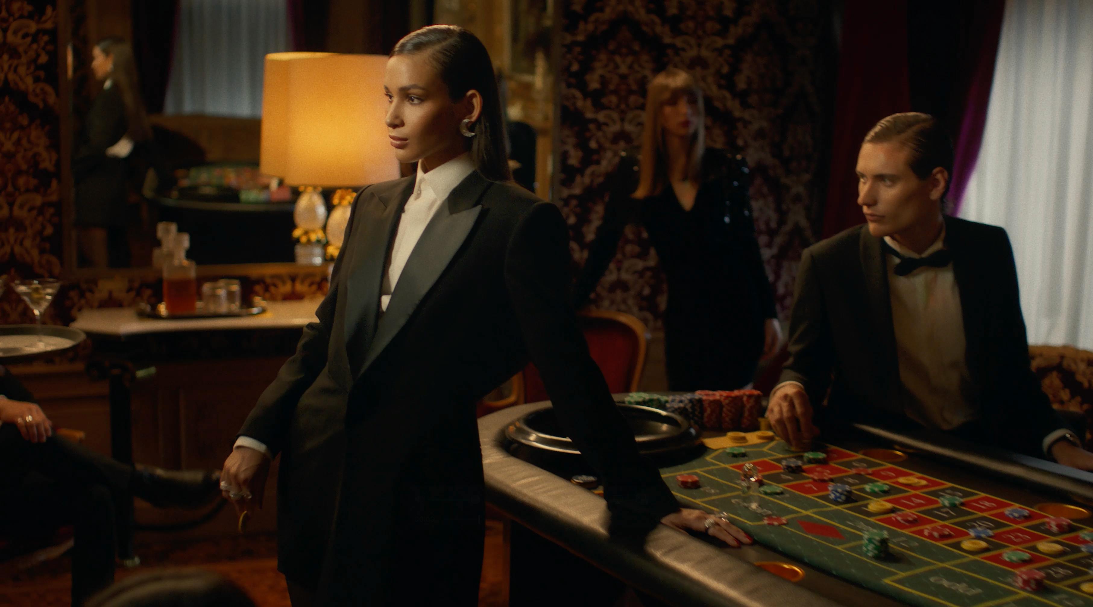 A person in formal wear stands in a dimly lit, elegant room.