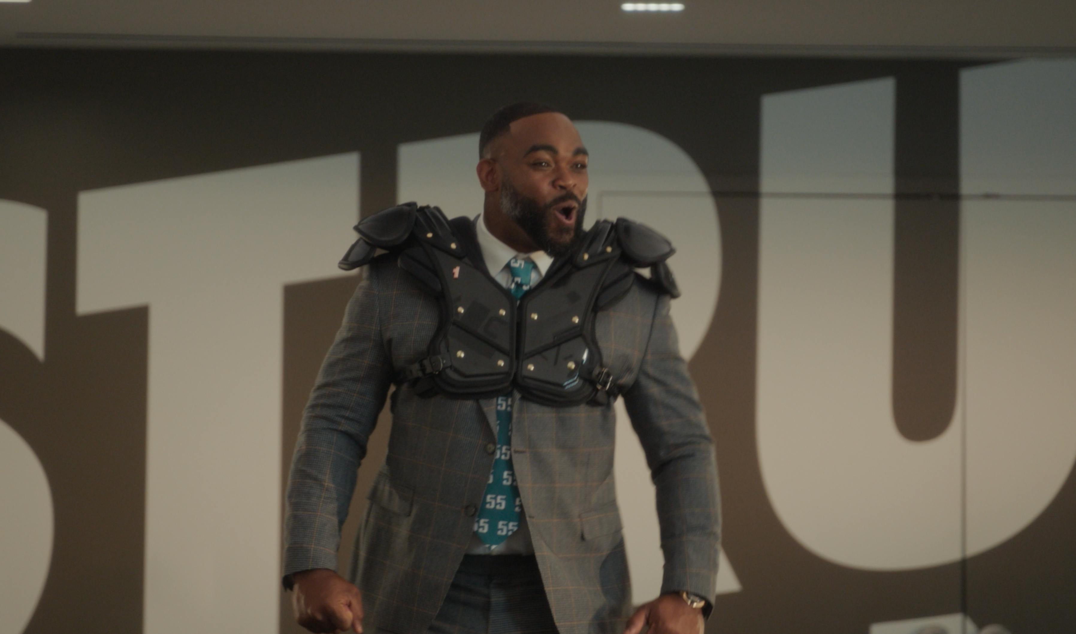 A man in a heavy coat stands in a dimly lit, industrial-looking hallway or urban setting.