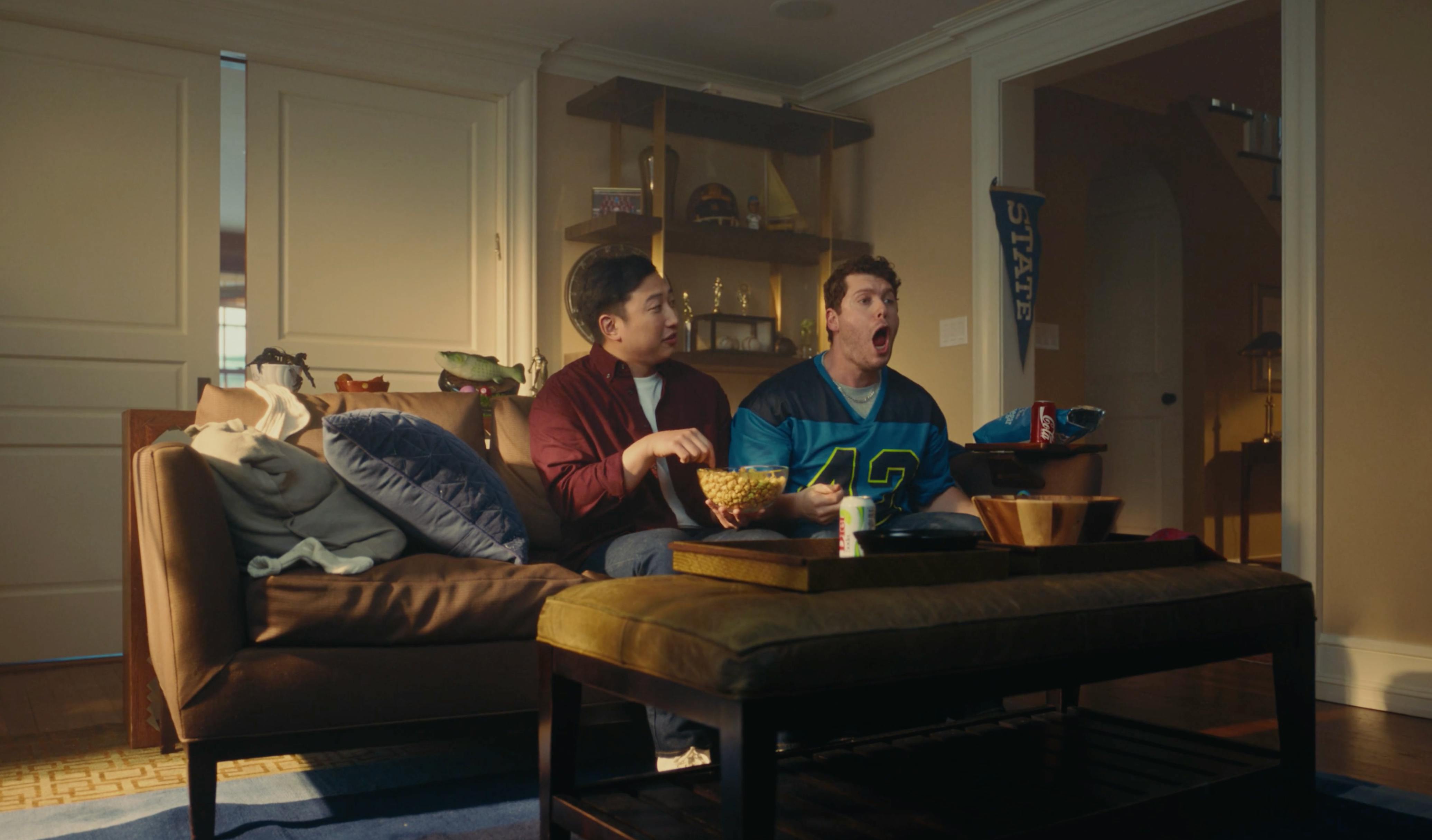 Two men watching TV on a couch with snacks, capturing audience engagement and storytelling in modern video production and creative media content