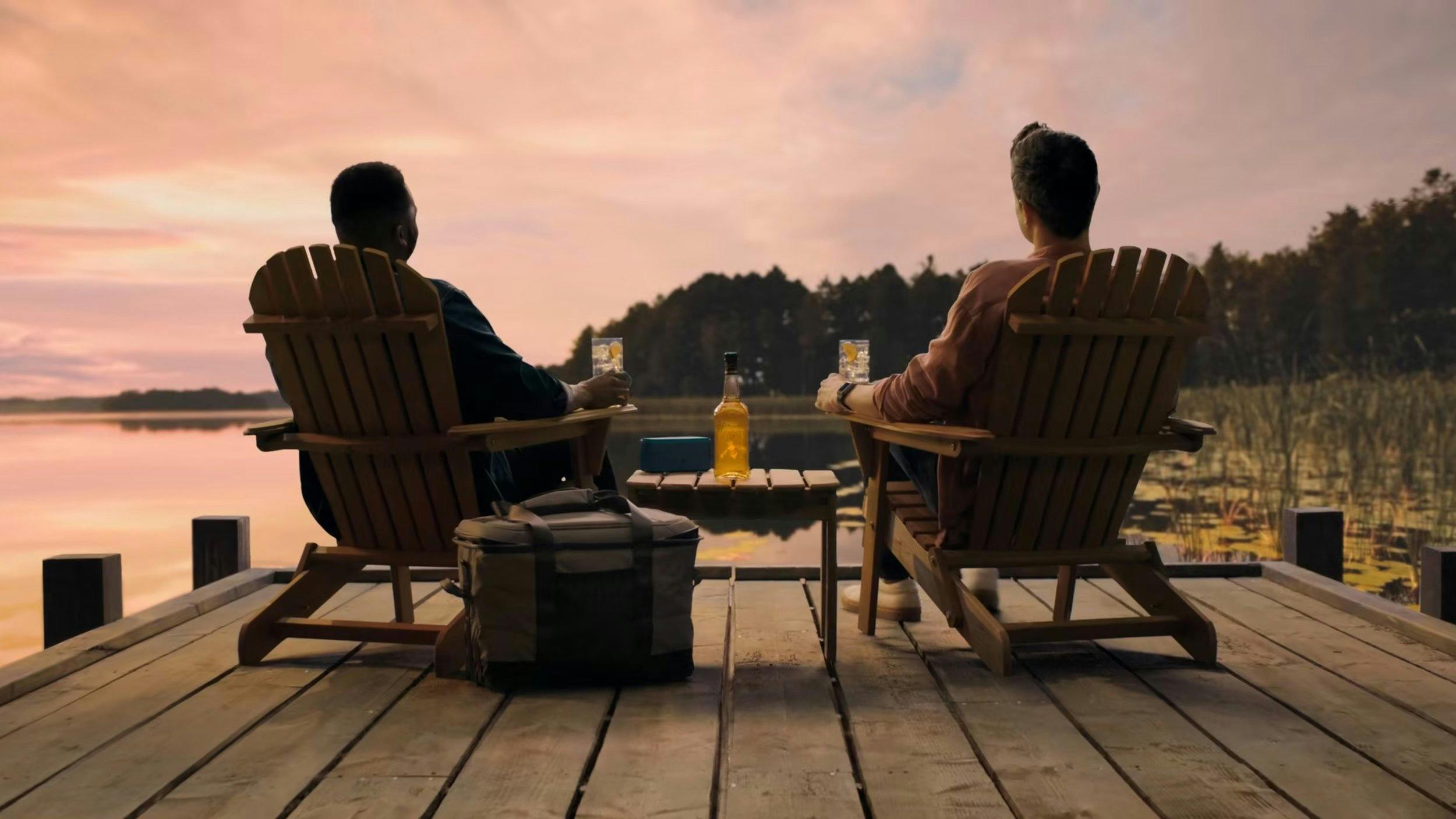 Wide shot of two men in Adirondack chairs on a dock at sunset. Cinematic lighting, high dynamic range, and perfect color grading for a luxury brand commercial or travel vlog.