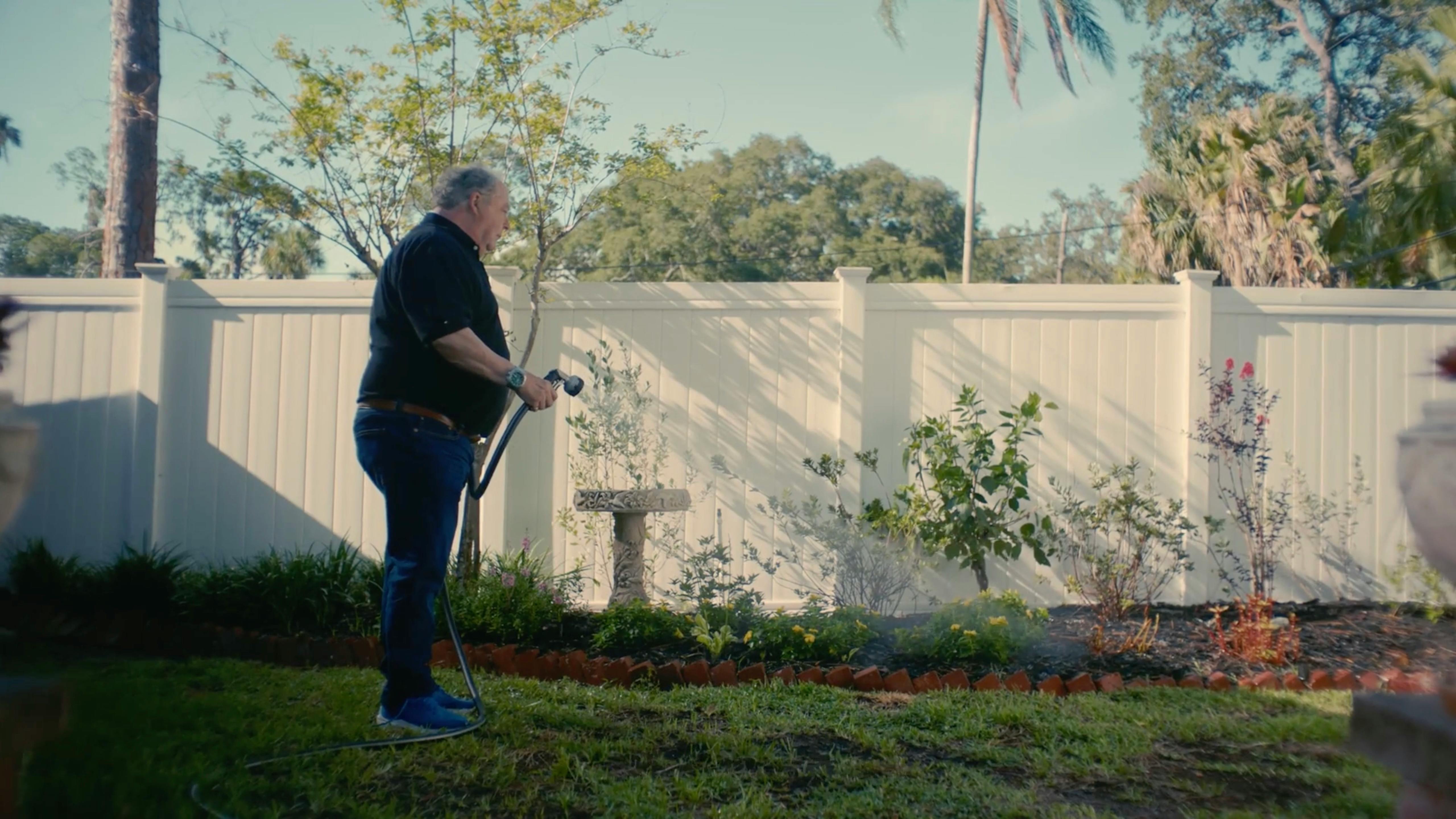 Man watering lawn outside a white fence home, filmed by a Miami video production company offering full service commercial video production film services