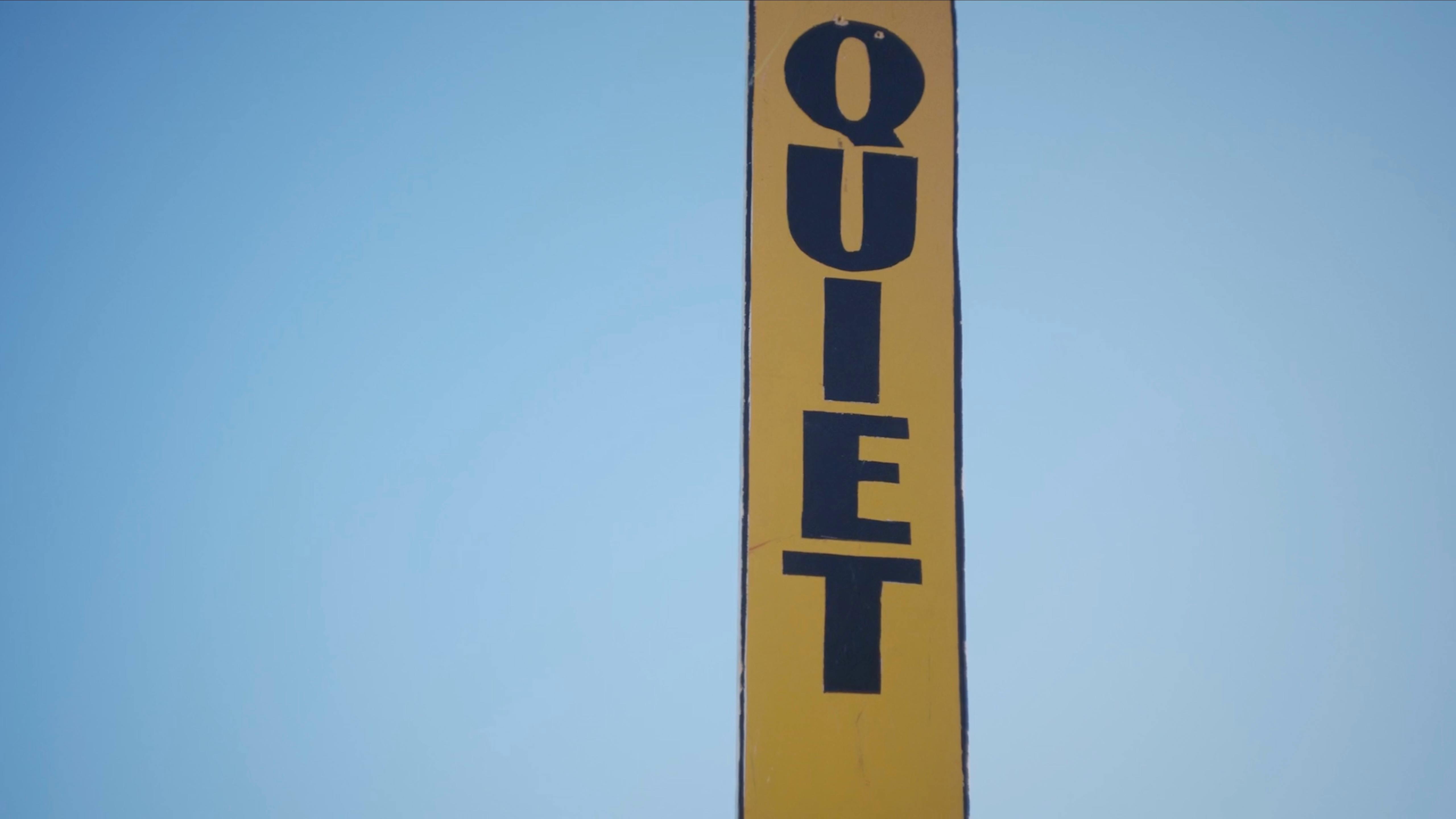 Tall roadside QUIET sign against blue sky in a photography for ads campaign concept